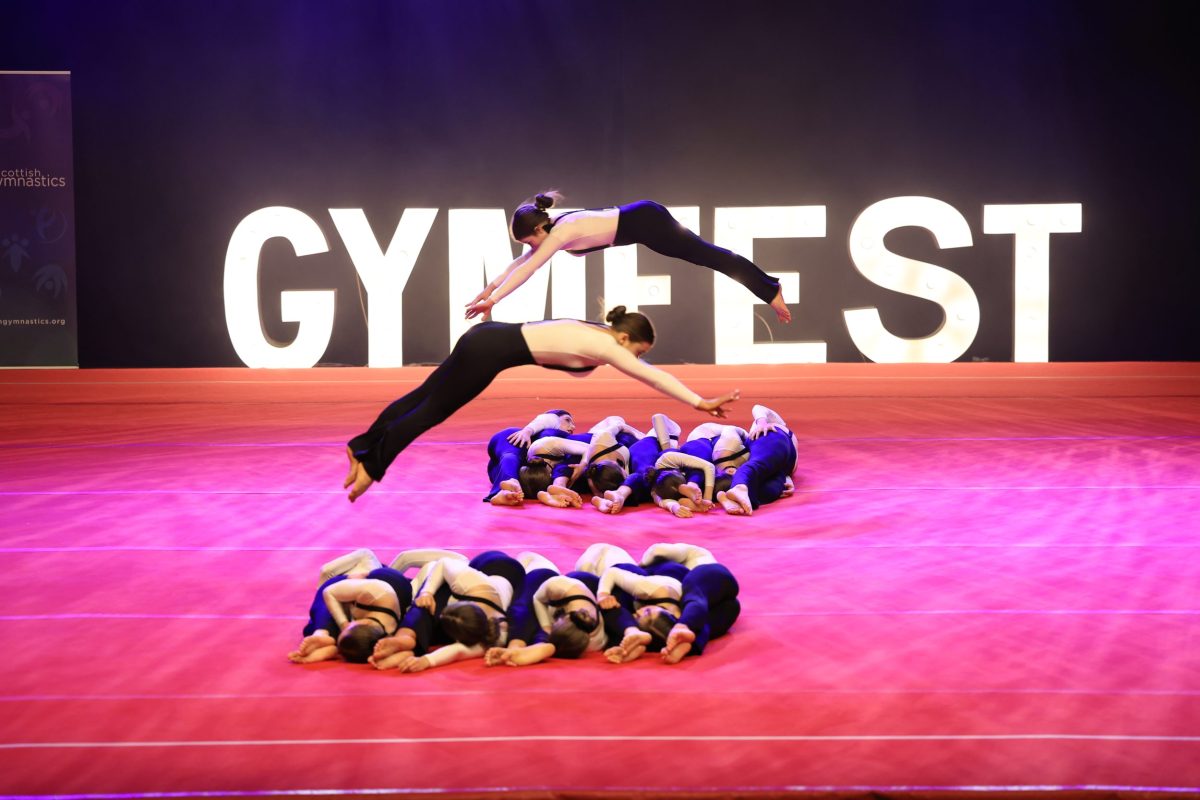 Two gymnasts perform dive forward rolls over their teammates at the Gymfest Display Event in Aberdeen in April 2022