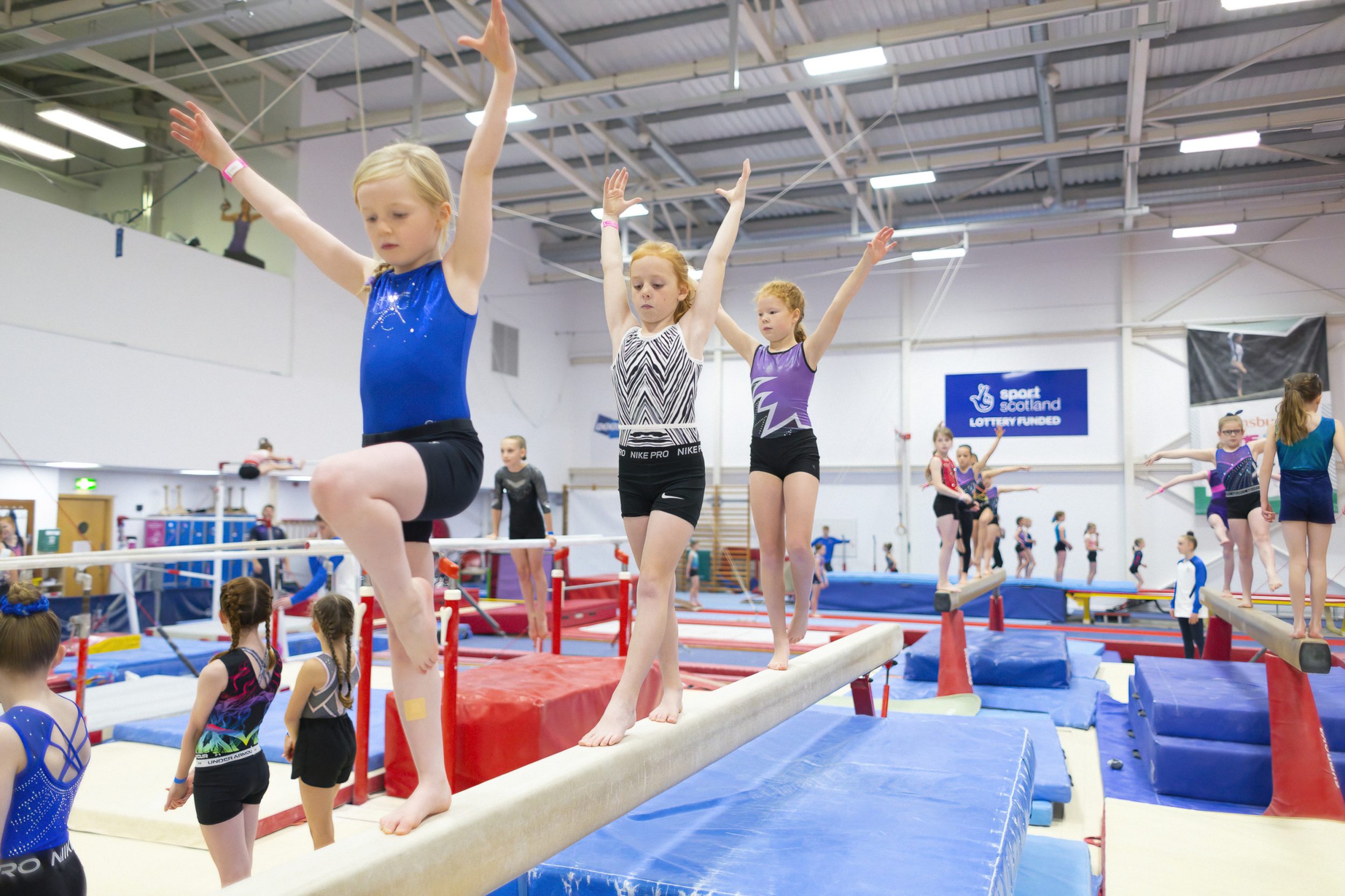 Three women's artistic gymnasts train on the beam at the 2022 commonwealth expereince day