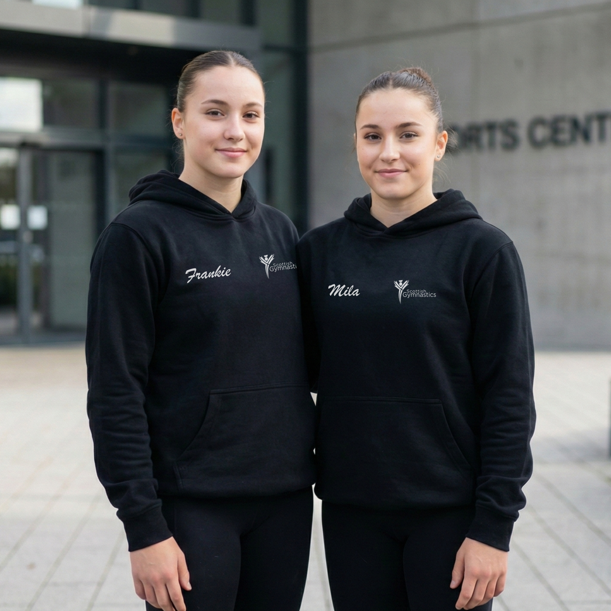 Two females together wearing the 2026 Scottish National Gymnastics Championships hoodie outside a sports centre.