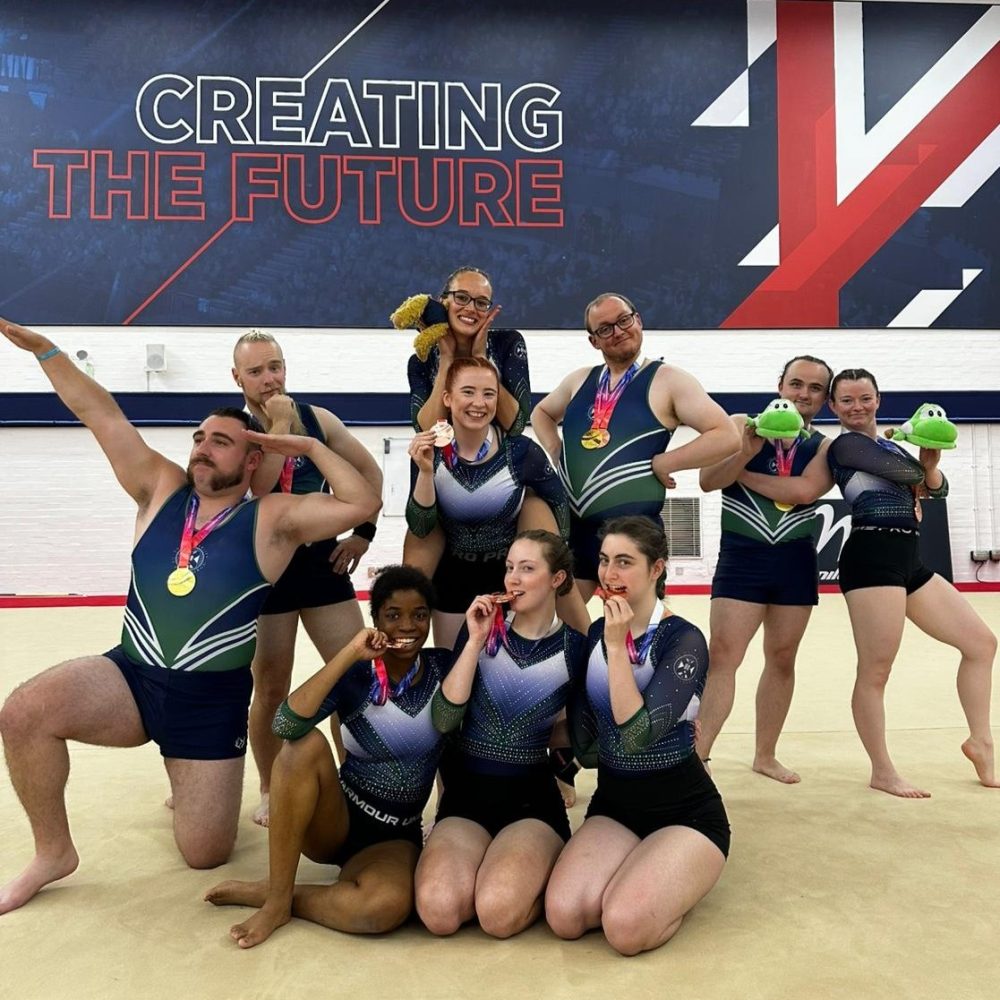 Group of male and female gymnasts from Edinburgh university posing in different ways with their medals at the 2025 Adult British Championships