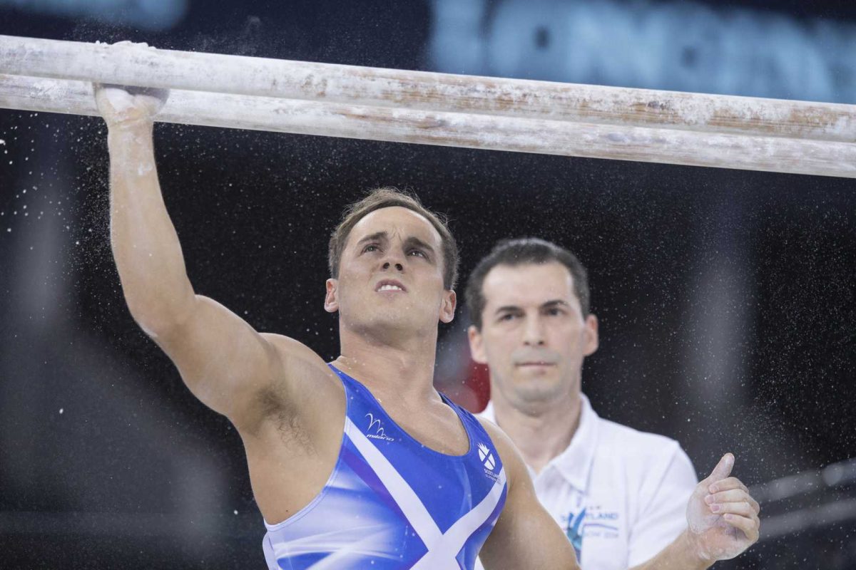 Team Scotland gymnast Dan Keatings putting chalk on parallel bars during Commonwealth Games watched by coach Marius Gherman